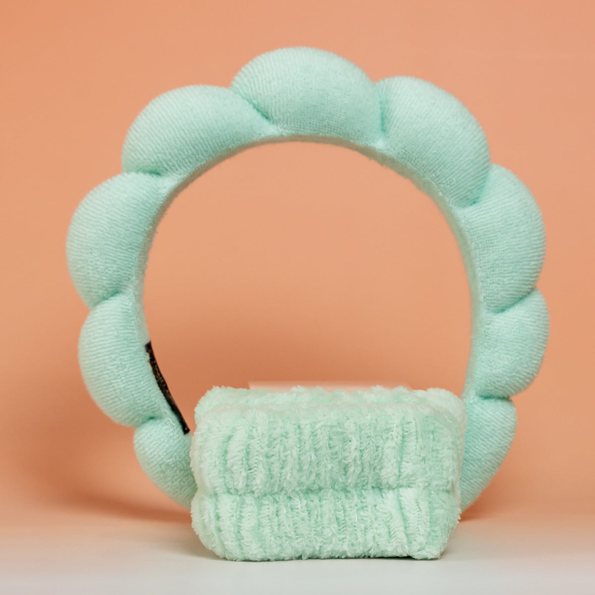 Bandeau de soin matelassé et poignets assortis BLUSH en tissu éponge vert menthe, présentés sur un fond rose et orangé.