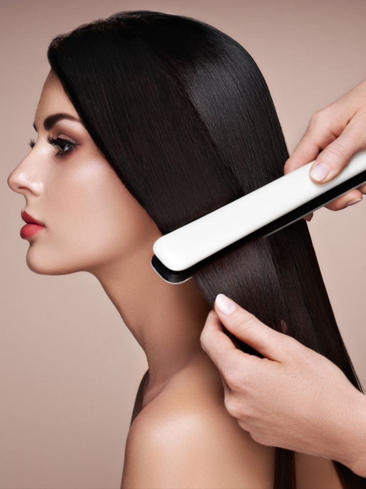Profile view of a woman with smooth, shiny, and repaired-looking hair while a flat iron gently glides through her hair, showing a sleek styling result